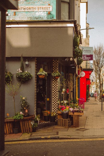 The image shows the exterior of a floral shop with an inviting display of fresh flowers arranged in various bouquets and potted plants. The flowers include vibrant pinks, whites, and greens, with rose