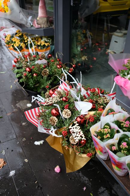 A collection of festive floral bouquets arranged with a mix of greenery, red berries, small pinecones, and shiny red baubles, wrapped in colorful paper with some accented by white and red striped ribb